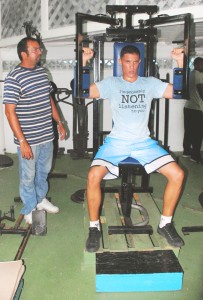 Niall Roberts does gym work at the Michael Parris Fitness Centre in the National Park watched closely by his coach Seon Baksh. (Clairmonte Marcus photo)