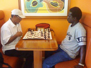 William and Nisa Walker, proprietors of the Oasis and Oasis Too cafes, in association with Young’s bakery, sponsored a knockout rapid chess tournament with a difference. Sixteen players emerged from the initial round to form four select groups. The winner of the preliminary round was veteran Learie Webster who played unbeaten, and is a favourite to win the tournament. The top four finishers of the four groups played a semi-final round, and the final was played last evening at the Oasis cafe in Carmichael St. The winner walked off with $40,000 and the runner-up got $20,000. In picture, Webster is relaxed as Tiwari studies the board. Webster, in his usual way, launched a blistering attack on the white pieces from which Tiwari never recovered.