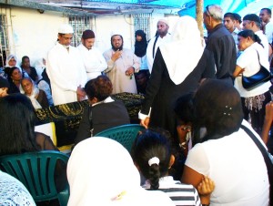 Moulana Abu Bakr Haniff (standing third from left), addressing the gathering while Alli’s close relatives sit around the coffin that was draped with a black cloth bearing gold inscriptions in Arabic.