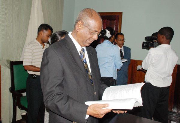 Speaker of the National Assembly Ralph Ramkarran (foreground) peruses the report while Auditor General Deodat Sharma (background) addresses members of the media. 