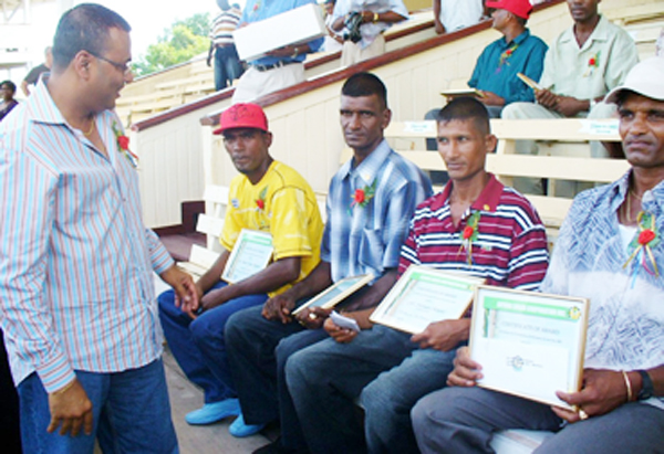 Minister of Agriculture, Robert Persaud (left) checks out the awards presented to the champion workers of the four Berbice estates. Sitting from left to right are Satesh Sanchara of Rose Hall, Sharma Persaud of Albion, Narendra Ramphal of Skeldon and Bhaiskoomar Samaroo of Blairmont.  