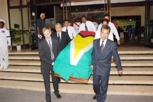 Pall bearers, including the son and son-in-law (right and left respectively) of Guyana’s first president Arthur Chung, carry the casket bearing his remains out of the National Cultural Centre to be taken to the Botanical Gardens for interment at the Seven Ponds. (Jules Gibson photo) 