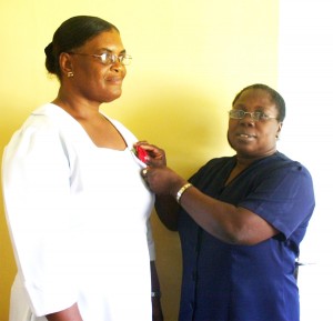 Senior Health Visitor, Deslyn Fraser (right) pins a token on Nurse Donna Fraser in appreciation of her dedicated services. 