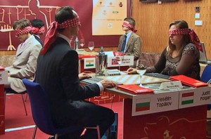 At the beginning of the game, players are required to wear blindfolds. Players record their moves by calling them out. The blindfolds are subsequently removed and the game continues without pieces on the chessboard. In picture, Topalov and Polgar begin their game.