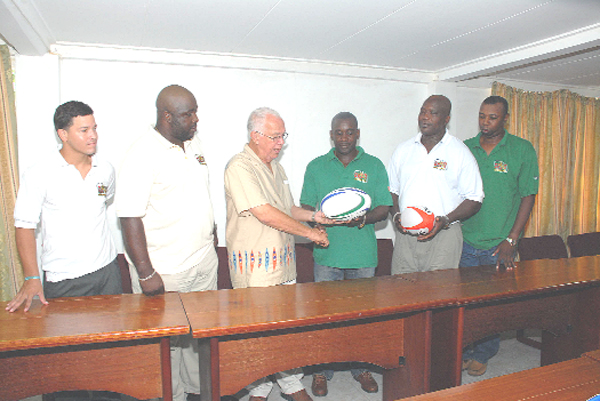 ‘Reds’ Perreira presents one of the two rugby balls to GRFU member Robin Peters while senior male and female national coaches Sherlock Solomon (2nd right) and Alton Agard (far right) look on along with GRFU Secretary Curtis Jackson (2nd left) and national male player Ryan George.