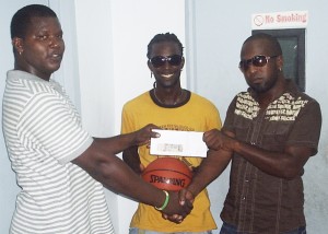 Representative of Slingers Enter- tainment, Shermon D’anrade aka ‘Dj Gringo’ (left) presents an envelope containing $100,000 to President of the Royals Basket-ball Club Glad-win Albert (right) in the presence of club captain Qwesi Joseph. (A Kiev Chesney photo)  