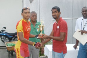 Henry Rambarran jnr., presents Alonzo Greaves, left, with the first place trophy on behalf of the sponsors. At centre is national cycling coach and race organizer, Hassan Mohammed. (Aubrey Crawford photo)