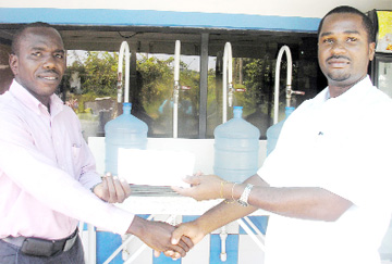 General Manager of the Oasis Water Company and Vice President of the Georgetown Football Association Wayne Ford (R) makes a presentation to Vice President of  Fruta Conquerors Marla Cole (L) in aid of a supply of water for the tournament.