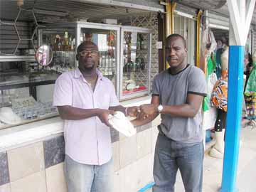 General Manager of  Junior’s Jewellery,  Ferdinand Bacchus Jnr. (L) hands over a gold chain,  which will be presented to the highest  goal scorer, to Marlan Cole.