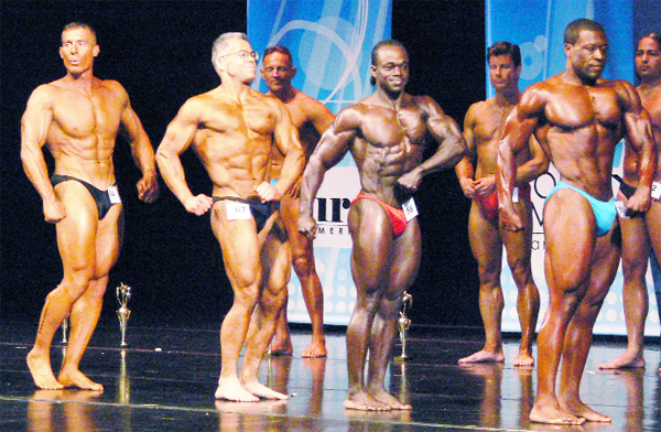 ALL THAT GLITTERS IS GOLD! Guyana’s Sylvan Gardner, fourth from right, is the centre of attention during the posedown on his way to capturing the overall title at the New York MuscleMania Superbody last Saturday. (Photo courtesy of Gary Tim.)  