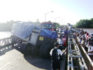 Pedestrians watch the damaged truck and car as another truck arrives to try to move the first truck. It failed and another truck equipped with a mini-crane had to be summoned to this accident on the Demerara Harbour Bridge yesterday.  