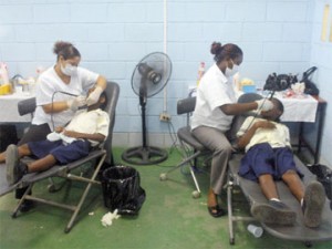 Two workers from the Cheddi Jagan Dental School working on giving two students from the North Ruimveldt Multilateral School bright smiles and healthy mouths yesterday during their outreach at the school.