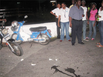 Onlookers at the scene of the Vlissingen and South Road accident; blood stains are evident on the road while the motorbike involved in the accident is braced on the culvert. 