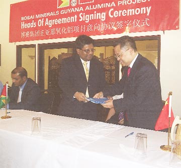 Minister of Finance, Dr Ashni Singh (left) and Managing Director of Bosai, Zhilun Yuan exchange documents after the Heads of Agreement signing ceremony yesterday. At extreme left, seated is President Bharrat Jagdeo. 