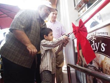 CEO of Nasir and Nasir, Naeem Nasir helps his son cut the ribbon to open the new parlour. In the background is Elias Munoz, Business Export Manager of Nestle, Caribbean. 