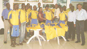  Gloria Tiwari presents one of the jerseys to Western Tigers’ Club Secretary Dexter Cush (centre) yesterday while members of the BK International Western Tigers team display their jerseys and trunks.