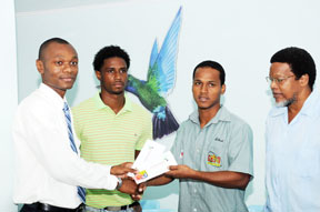 Here you go guys…Lead agent of Caribbean Airlines Dion Inniss (left) hands over the tickets to Albert La Rose (second right) while Claudius Butts (centre) and president of the Guyana Rugby Football Union (GRFU) Noel Adonis (right) looks on appreciably. (Clairmonte Marcus photo) 
