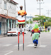 Two members of a masquerade band working the streets yesterday in keeping with the seasonal feature, as captured in their flouncing. Photographed here are Bam Bam Sally (backing the camera) and a flouncer on stilts. (Jules Gibson photo) 