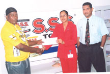 Billing Clerk of Geddes Grant (Guyana) Limited, Berbice branch, Roxanne Pahalad hands over the sponsorship cheque to Flying Ace Cycle Club Coach Randolph Roberts while Branch Manager Wazim Ali looks on. 