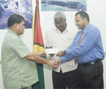 President of the Guyana Cricket Board Chetram Singh (left) hands over a cheque of US$750,000 on behalf of the West Indies Cricket Board, to Minister of Culture, Youth and Sport Dr. Frank Anthony (right) while Permanent Secretary Keith Booker shares the moment. (An Aubrey Crawford photo) 