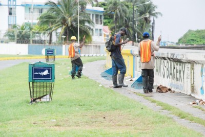 Workers removing litter on the seawall yesterday after the weekend and holiday festivities. Note the empty bins which the garbage should have been placed in but was not. (Photo by Jules Gibson)