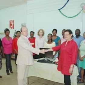 British High Commissioner Fraser Wheeler hands over the computers to Denise Dias. Representatives of Help & Shelter are in the background.