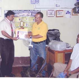 Treasurer of the Berbice Cricket Board of Control (BCBC) Anil Beharry hands over the certificate and trophy to Hubern Evans.  