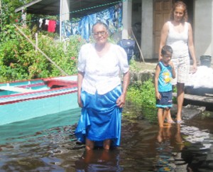 Dhanasari Mangal of Pine Ground, Mahaicony Creek in front of her flooded yard yesterday. Also in photo is her daughter, Youndai Adjuder who was visiting from California and a grandchild. 