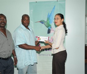 Mr. Guyana Mark Anthony Perry (left) receives his two airline tickets from Caribbean Airlines Sales Executive Kathleen Shuffler-Ten-Pow, whilst GABBFF president Frank Tucker looks on appreciably. (A Clairmonte Marcus photograph)     