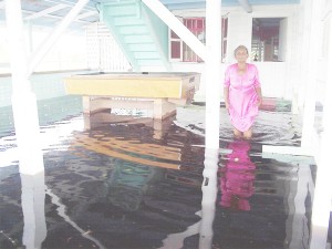 Rookmin Persaud shows the level of the floodwater at her shop in Little Baiboo, Mahaica Creek yesterday. She said that the pools table had been placed on drink cases but the water still reached it.  