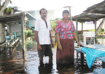 Gainda Persaud and his wife, Lakranie Durga [doing laundry] in front of their flooded yard.