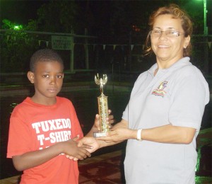 Dorado’s Head Coach Stephanie Fraser presents eight-year-old Daniel Scott with the mini-meet championship trophy.  