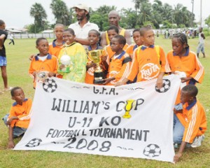 The Fruta Conquerors team poses with the Williams Cup Trophy after defeating Santos 1-0 in the final at Tucville Playfield yesterday. Coach, Kurt Cadogan stands at the back of his players. (Clairmonte Marcus photo)