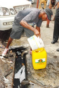 Filling up: This man made the best of the fuel spill yesterday as he dipped from the drain and poured into his jerry can 