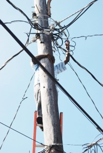 An employee of the Guyana Power and Light Company (GPL) snapping an illegal connection on a lamppost in Albouystown yesterday. (Photo by Jules Gibson)  