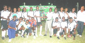 Camptown’s Captain Rashawn Sandiford is seen receiving the Milo Under-21 Trophy from a Beepat’s Marketing Assistant Selwyn Bobb (centre) as the team and coaches shared the historic moment at the Tucville Playfield after becoming the inaugural champions. (Orlando Charles photo) 