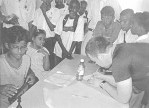 Grandmaster Buhmann signs the scoresheet for Queen’s College student Cecil Cox. Cecil was the last player to go down to the grandmaster, stretching him for 60 moves before succumbing to a piece down. He gained the admiration of his fellow students, the grandmaster, teachers, parents and others who witnessed the exhibition. Cecil held the grandmaster for close to three hours. In photo at left, is Cecil watching the grandmaster intently. On his left is Ashley Anthony, daughter of the Minister of Sport, Dr Frank Anthony, who also played in the exhibition.    