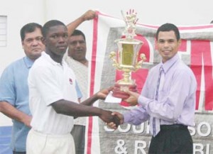 Berbice’s skipper and national Under-19 wicketkeeper Anthony Bramble receives the championship trophy from Chief Executive Officer (CEO) of GTM, Roger Yee, whilst president of the Guyana Cricket Board Chetram Singh (left) looks on. (Orlando Charles photo)  