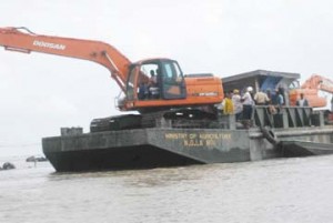An excavator mounted on a pontoon dredges the mouth of the Abary River 