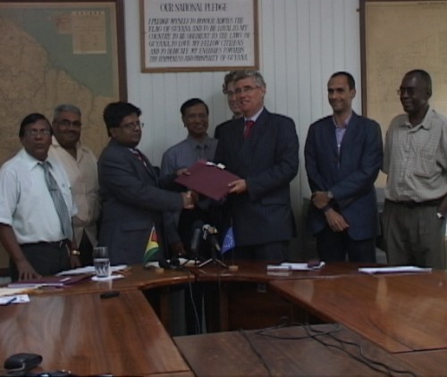 Minister of Finance, Dr. Ashni Singh, and Head of the EU delegation to Guyana, Geert Heikens, shake hands after the signing of the agreement. Staff of the Ministry of Finance, the Lands & Surveys Commission and other members of the European Union delegation look on (gina.gov.gy Photo)