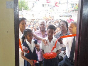 The ribbon being cut to launch the reading/computer room. From left in second row are Headmistress of Montrose Primary, Padmouti Puran, Head of Food for the Poor (Guyana) Leon Davis, Hazel Answich of the Region 4 Department of Education and Anthony Haunte, Community Involvement Specialist, Ministry of Education.