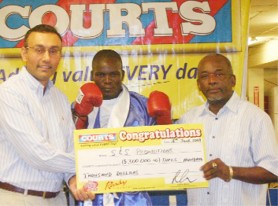 Courts Guyana Inc. Country Manager Lester Alvis (left) hands over their sponsor’s cheque to promoter Stanford Solomon (right) while Leon ‘The Lion’ Gilkes poses in the centre (Orlando Charles photo).