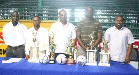 Director of Sport, Neil Kumar (centre) takes a photo opportunity with Banks DIH’s Lee Baptiste (2nd R), GFA President and Secretary Troy Mendonca (R) and Marlan Cole (L) with Competiton Coordinator Seville Ferreira (2nd L). They stand behind the top finishers trophies and special futsal balls. (Orlando Charles photo)    