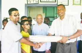 Ganesh Singh receives a quantity of stumps from Roger Harper while Minister of Home Affairs, Clement Rohee, looks on. 