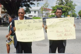AFC Leader Raphael Trotman (left) and Chairman Khemraj Ramjattan bearing placards yesterday outside of Parliament.  (Jules Gibson photo)