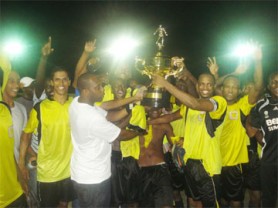 Alpha United’s captain Howard Lowe receives the championship trophy from one of the tournament organizers (centre) as team mates and supporters share the moment.