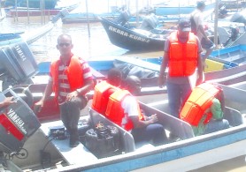 The three Guyana Defence Force Coast Guards sitting (centre) in the police boat yesterday before leaving for Caiman Hole in the Essequibo River where they reportedly dumped Dweive Kant Ramdass. 