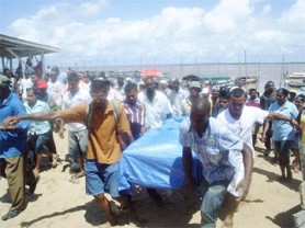 A crowd follows as the body of Dweive Kant Ramdass is moved from the Parika beach. His body was found floating at Caiman Hole in the Essequibo River yesterday morning.  