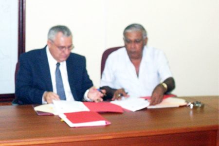 From left, representative of the Emergence Group Incorporated, US, David Bodi and Project Coordinator, Citizen Security Programme, Khemraj Rai sign the contracts. (GINA photo) 