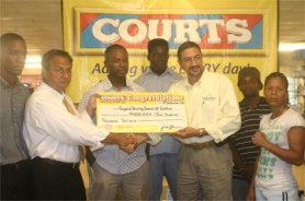 Purchasing Director of COURTS Guyana Inc. Clyde de Haas (right) presents the $400,000 cheque to President of the GBBC Peter Abdool as Carwyn Holland looks on in the middle. Also in the photo are boxers Shondell Alfred (right), Paul Lewis Jr. and Mitchell Rogers with Courts Public Relations representative Pernell Cummings (left).  (Orlando Charles photo) 